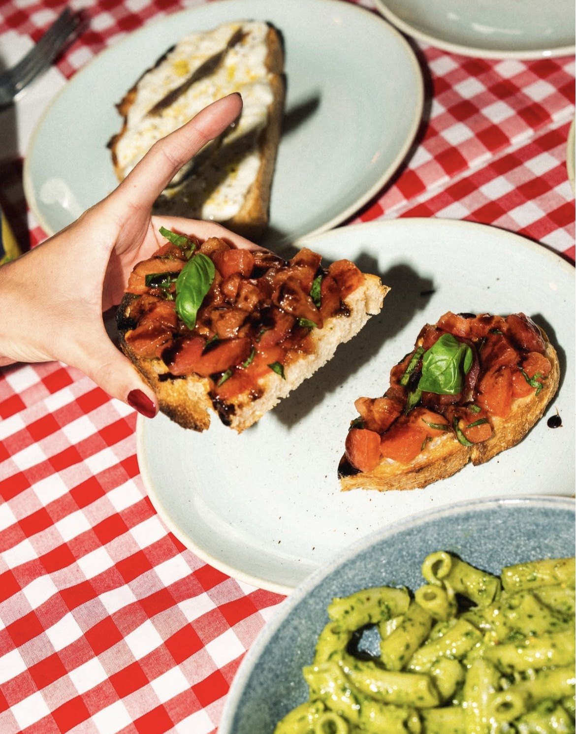 Bruschetta held in hand next to a bowl of pesto pasta